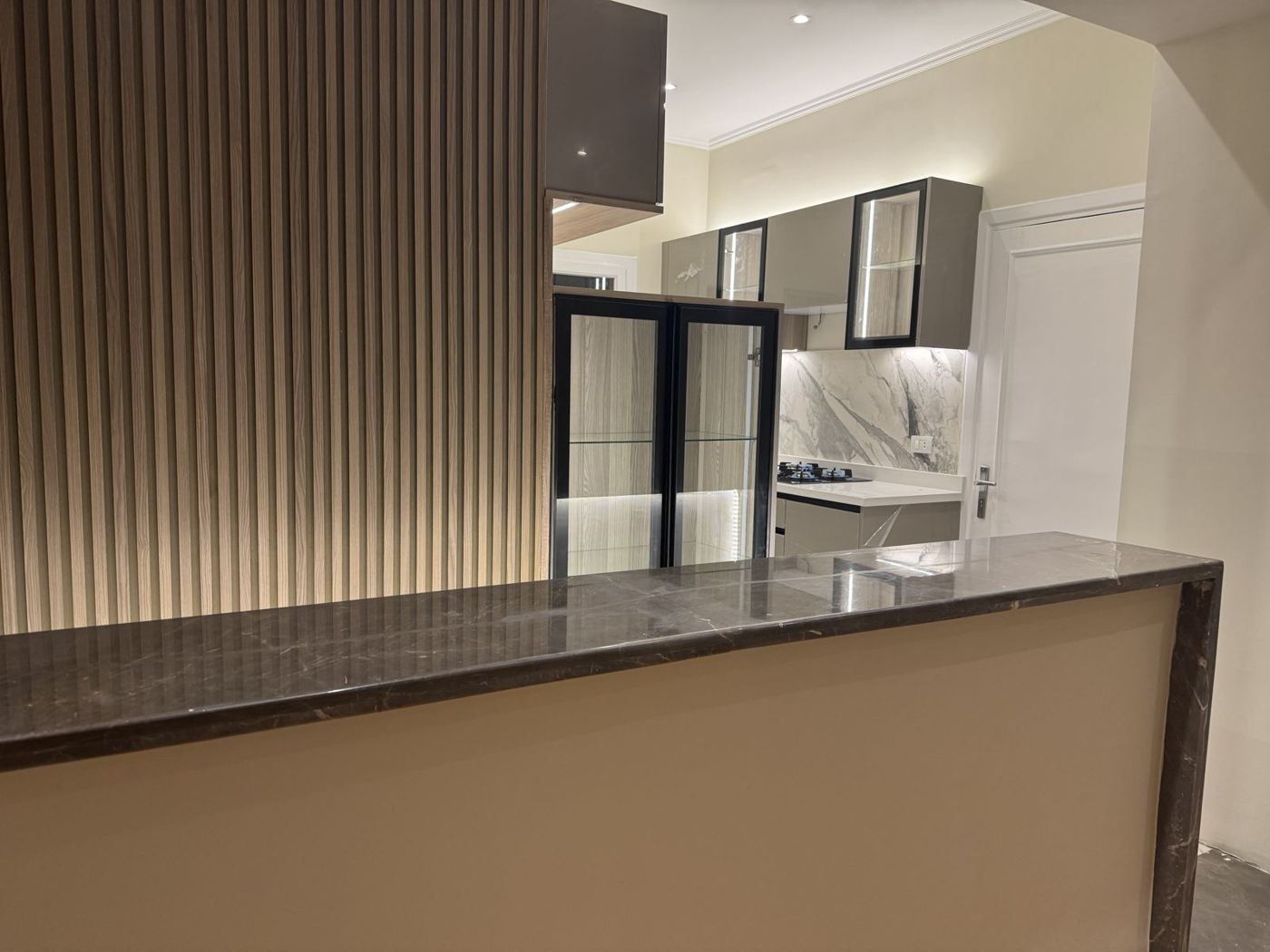 Taupe gloss kitchen with fluted wood wall and stone counter