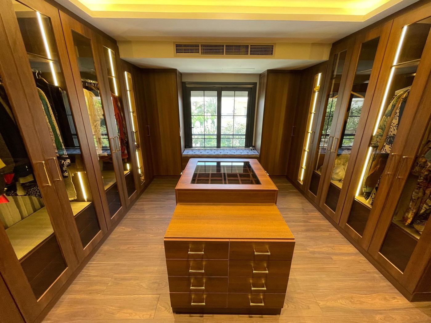 Walk-in dressing room with lit glass wardrobes and central island